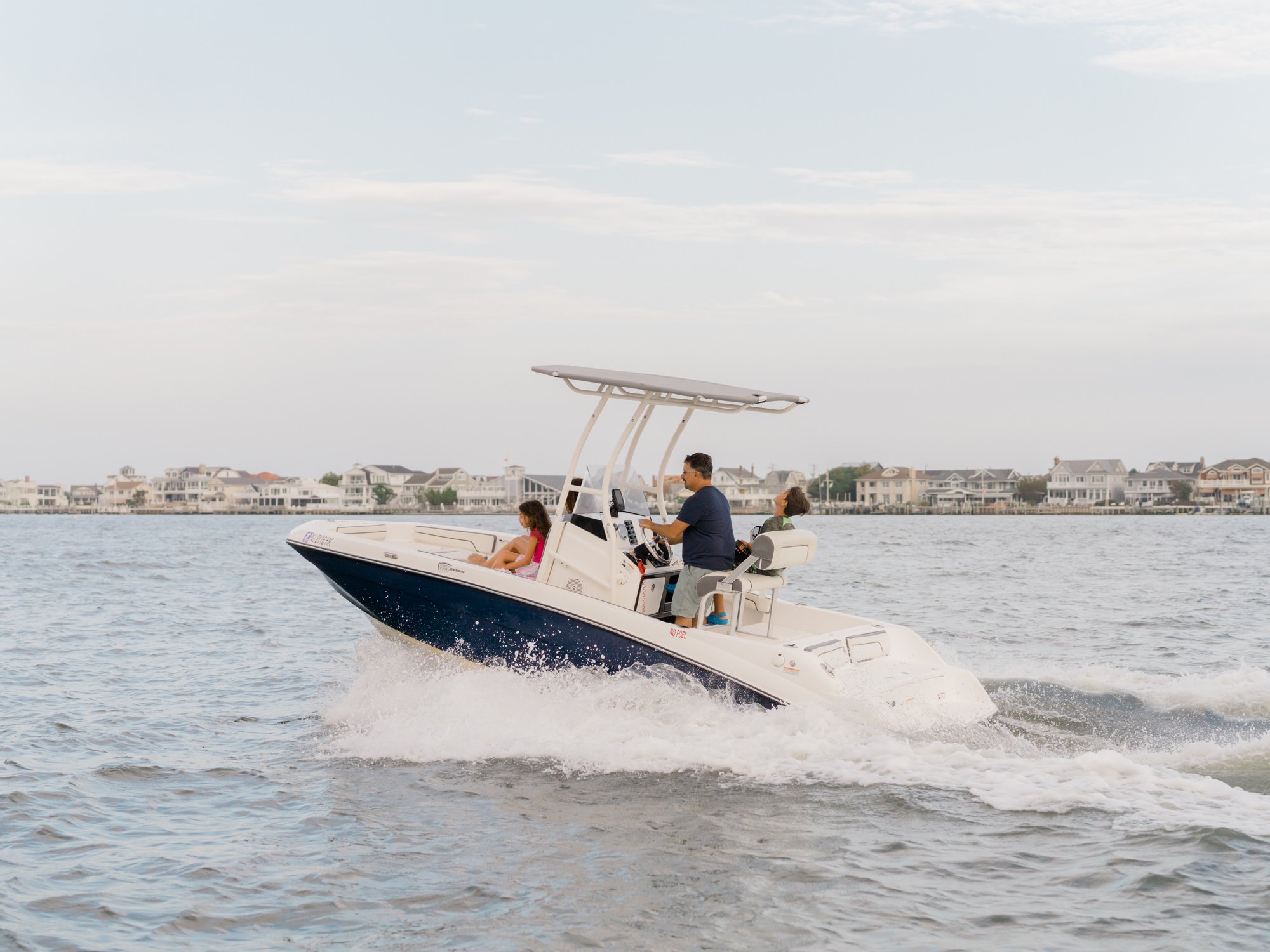Family running a Jet Drive Exchange center console boat across the bay near Ocean City, NJ with waterfront homes behind them